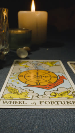 Vertical-Video-Close-Up-Shot-Of-Person-Giving-Tarot-Card-Reading-Laying-Down-The-Wheel-Of-Fortune-Card-On-Table